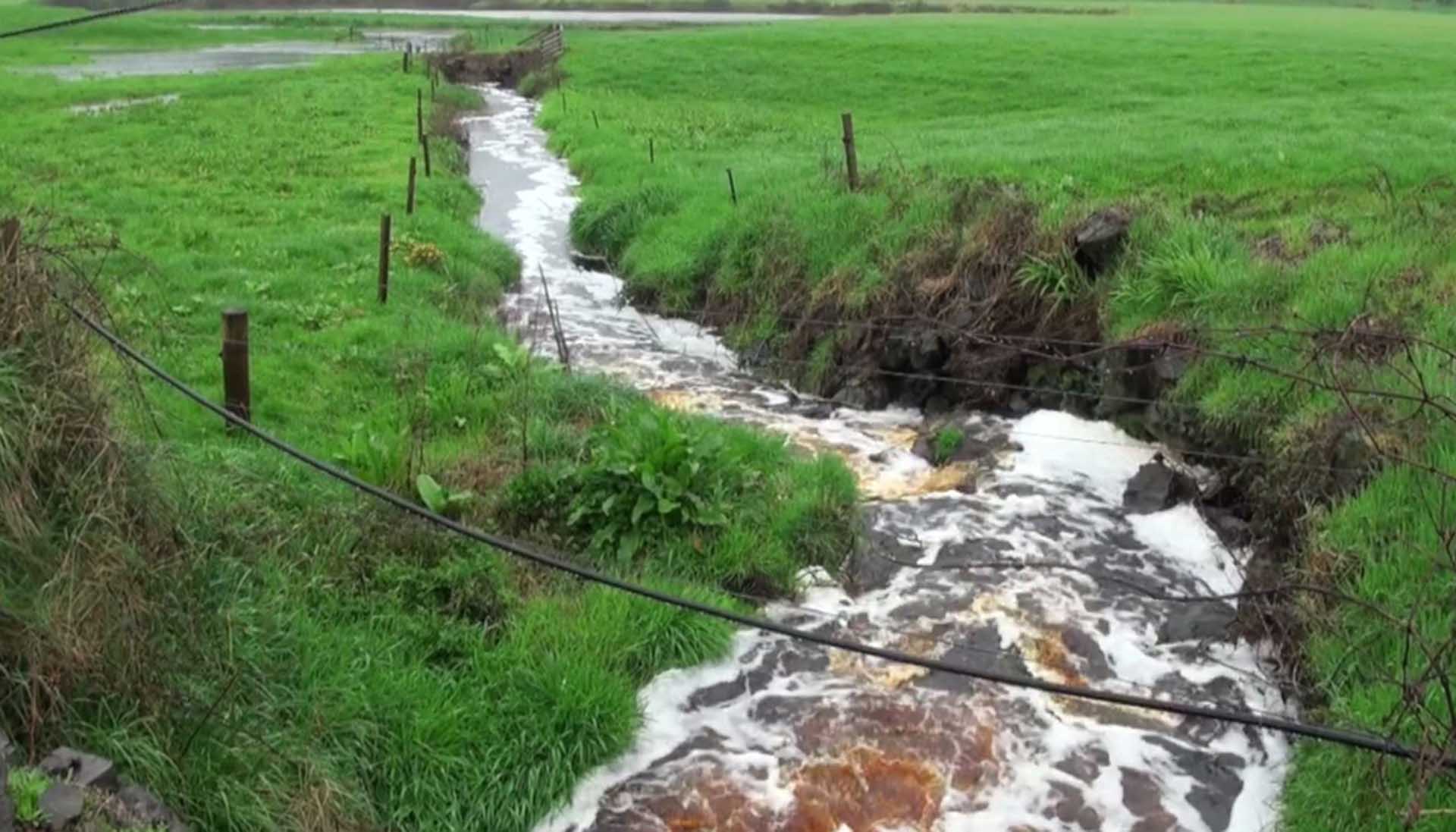 A turbulent, muddy river intersecting green fields on either side.