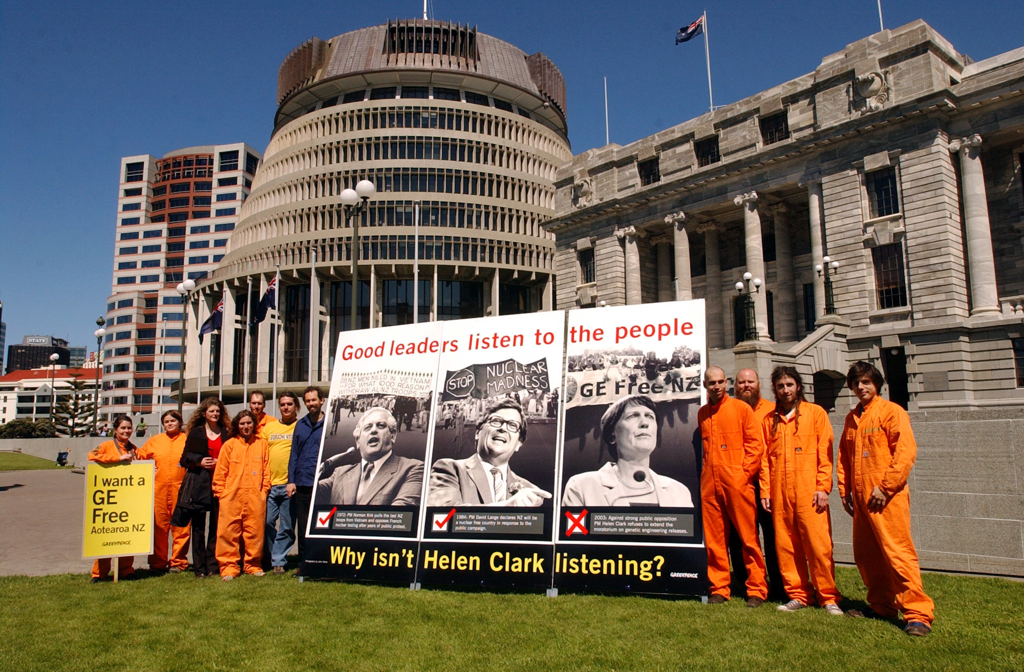 Greenpeace activists protest with a billboard outside the parliament in Wellington. Greenpeace is protesting the Labour Government's decision not to extend the moratorium on GE. The billboard is headed "Good leaders listen to the people" and depicts former Prime Ministers Norman Kirk and David Lange and current PM Helen Clark with historical images of anti-Vietnam, anti-nuclear and anti-GE protests corresponding to each PM with brief descriptions of the actions taken by the respective leaders.