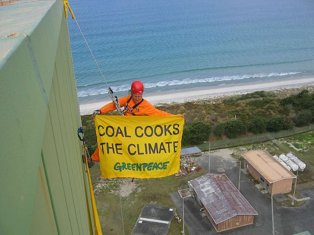An activist climbes the power station in protest with a banner reading "Coal Cooks The Climate"