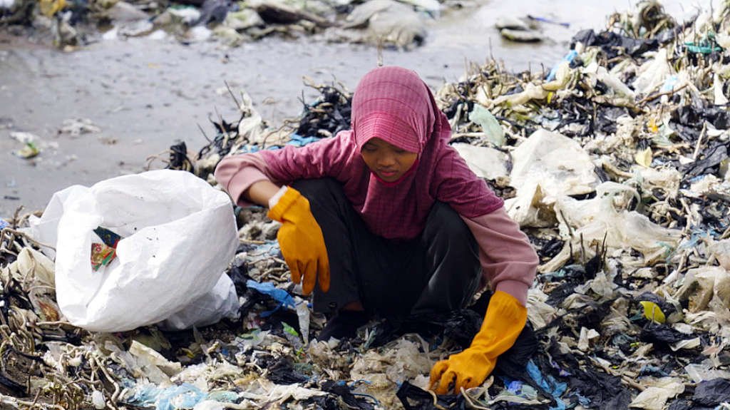 A girl with yellow gloves squats picking up plastic trash