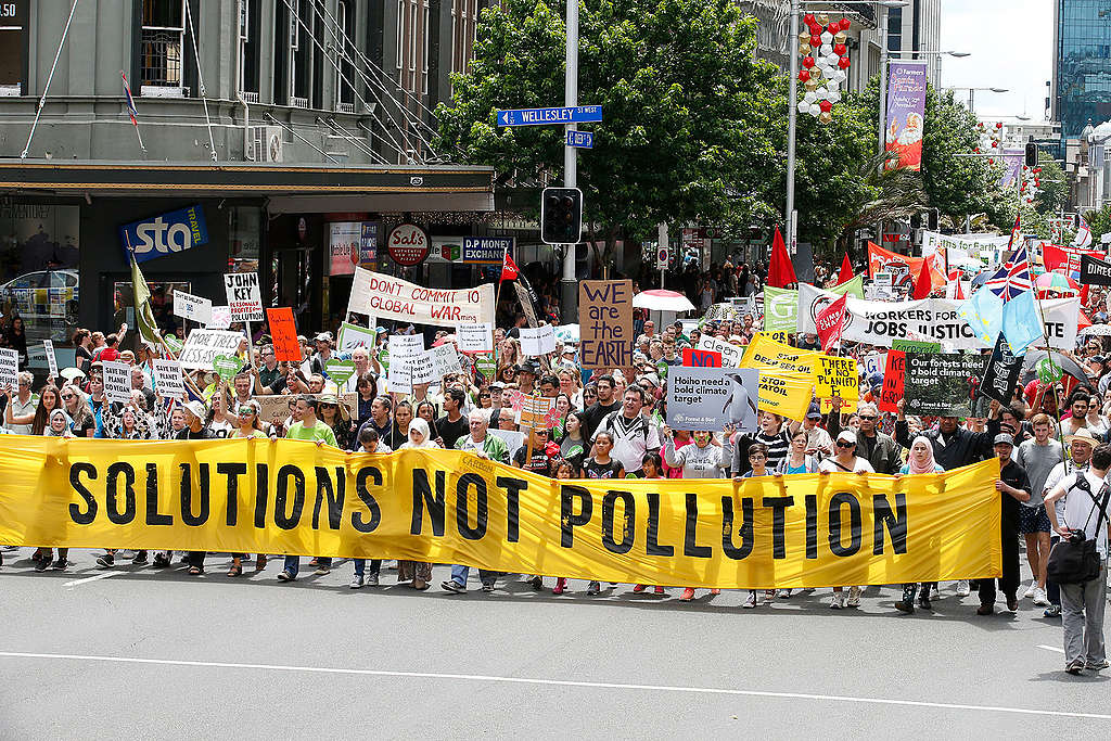 15,000 protesters marching up Queen Street, Auckland, carrying a large banner that reads 'Solutions not pollution'.