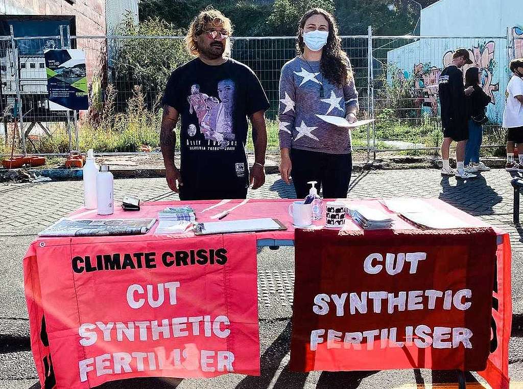 Two people stand behind a table with red signs that say Climate Crisis, cut synthetic nitrogen fertiliser