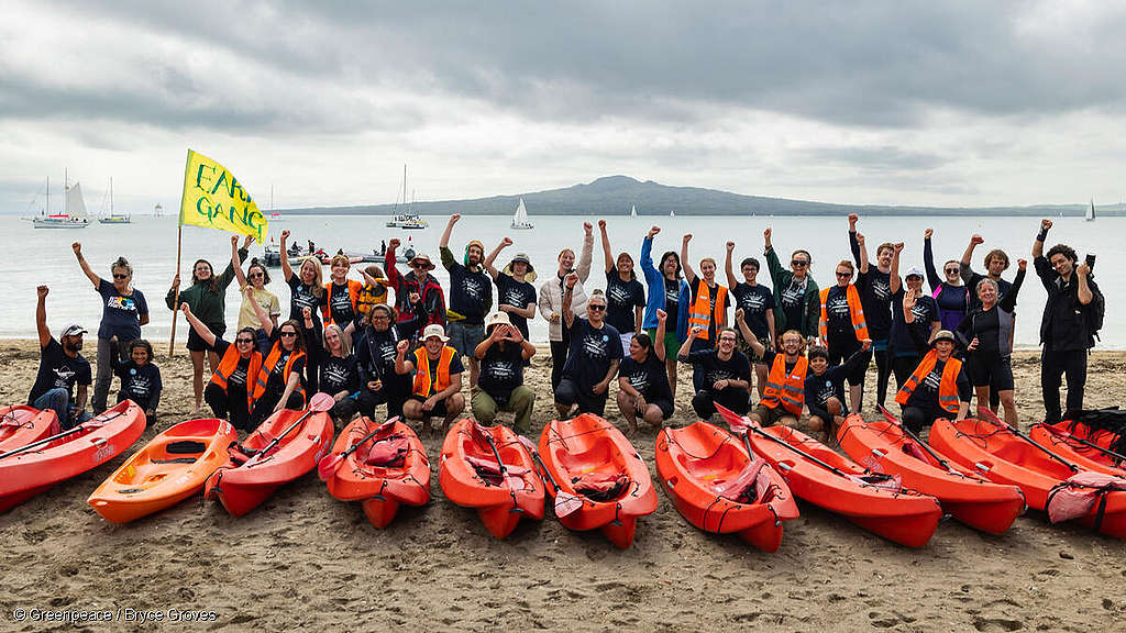 Kayakers against bottom trawling. A group of people with kayaks in the foreground wave to the camera with Rangitoto in the background