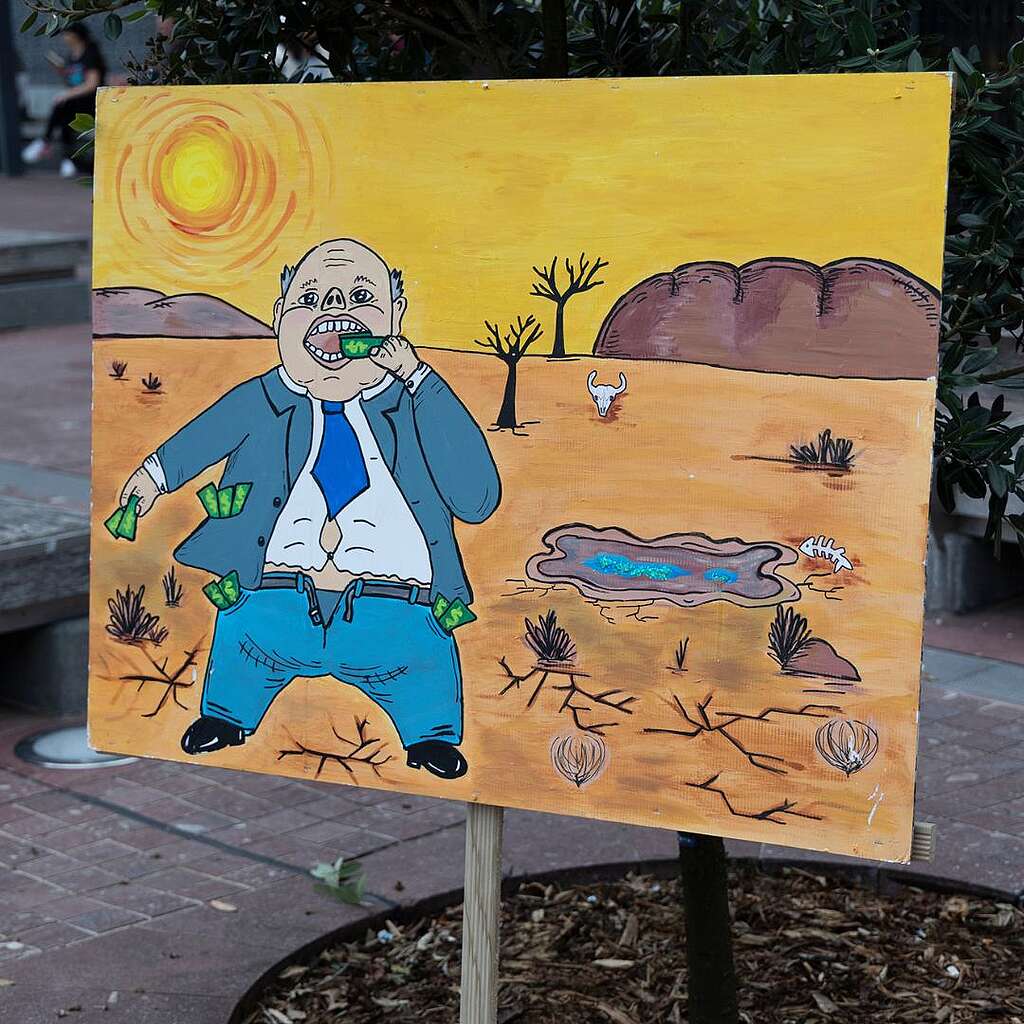 Placards from the March for Nature - A rotund person eats money with a barren landscape in the background