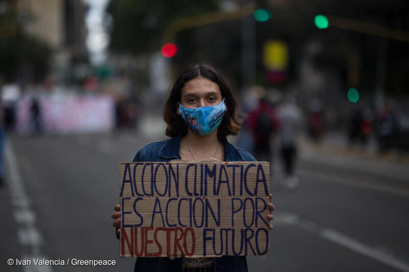 Activista en una marcha global por el clima en Bogotá, sostiene un cartel "Acción climática es acción por nuestro futuro".