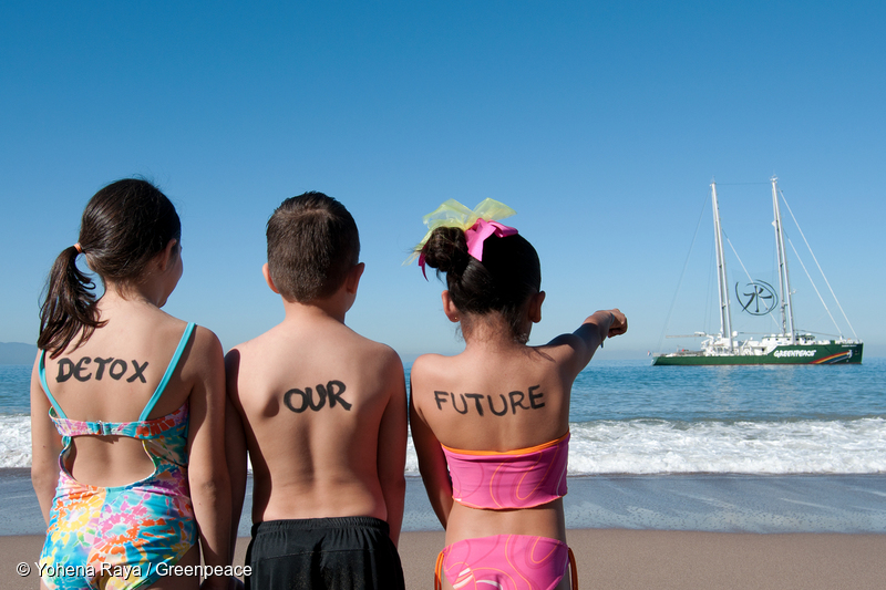 Los niños observan el barco de Greenpeace, Rainbow Warrior, que muestra el "símbolo Detox" entre sus mástiles.
