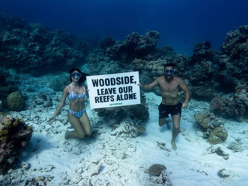 Los influencers Riley Whitelum y Elayna Carausu, de Sailing La Vagabonde, sostienen un letrero que dice "Woodside, deja en paz nuestros arrecifes