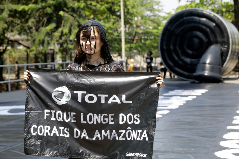 Ativista mulher do Greenpeace segura pintada com petróleo falso segura banner em protesto contra a petrolífera Total.