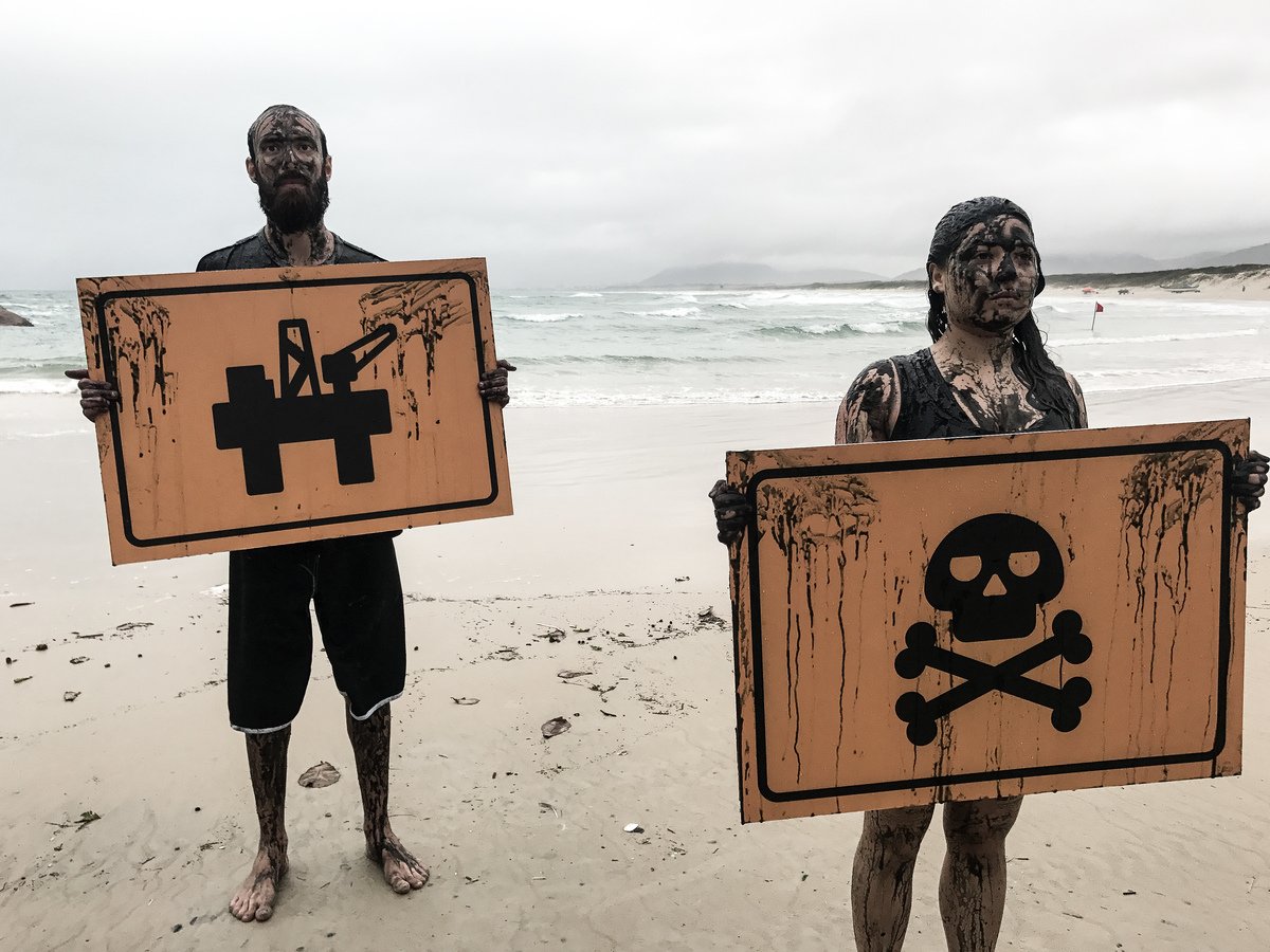 Voluntários sujo com petróleo falso do Greenpeace seguram placas com imagem de uma plataforma de petróleo e da morte.