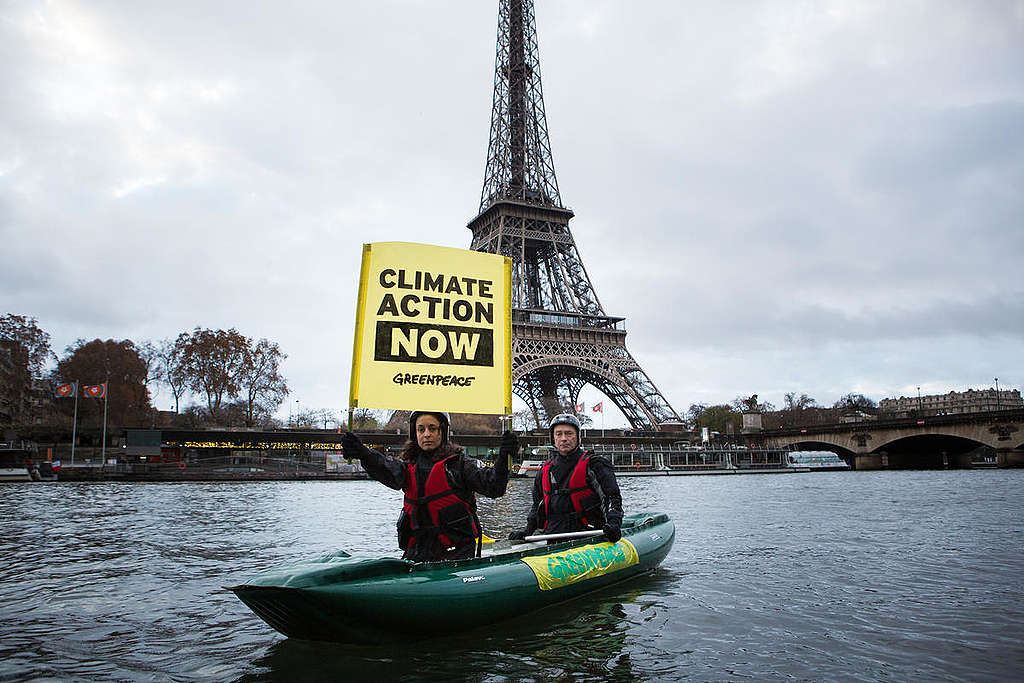 Ativista em caiaque segura um banner pedindo mais ação climática, em frente à torre Eiffel. © Jean Nicholas Guillo