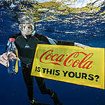 Mergulhador com garrafa plástica, segura um banner com a inscrição: Coca-Cola, isso é de vocês? © Justin Hofman