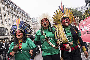 Pintadas de vermelho, com chocalhos nas mãos e usando cocares, Mulheres líderes indígenas entoam cantos durante protesto em Berlim