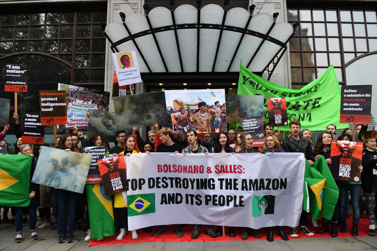 Ativistas protestam com faixas, cartazes e bandeiras do Brasil em frente á porta de entrada da Embaixada do Brasil em Londres