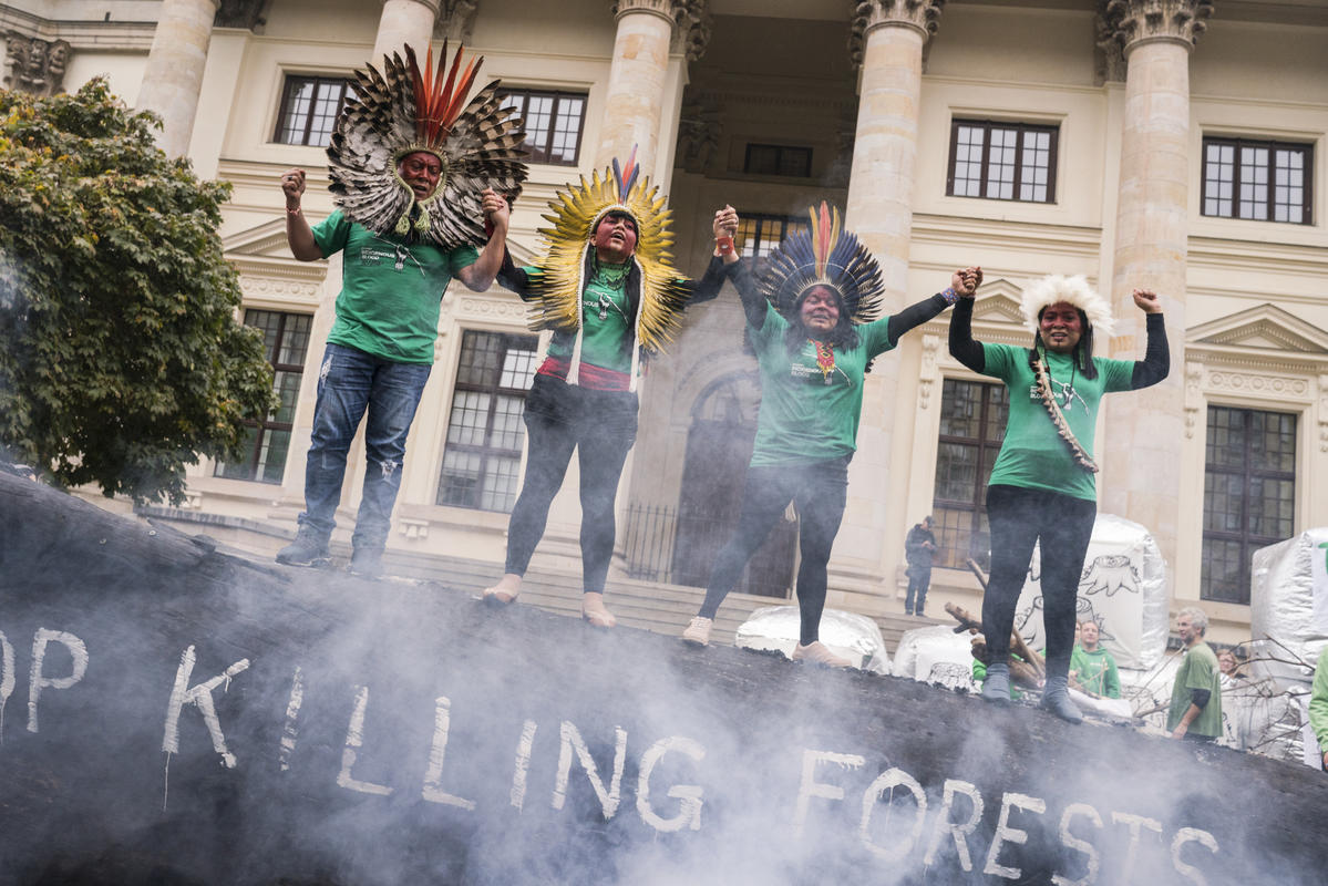 Quatro indígenas da comitiva da Jornada Sangue Indígena sobem em tronco queimado e dão as mãos em protesto em Berlim