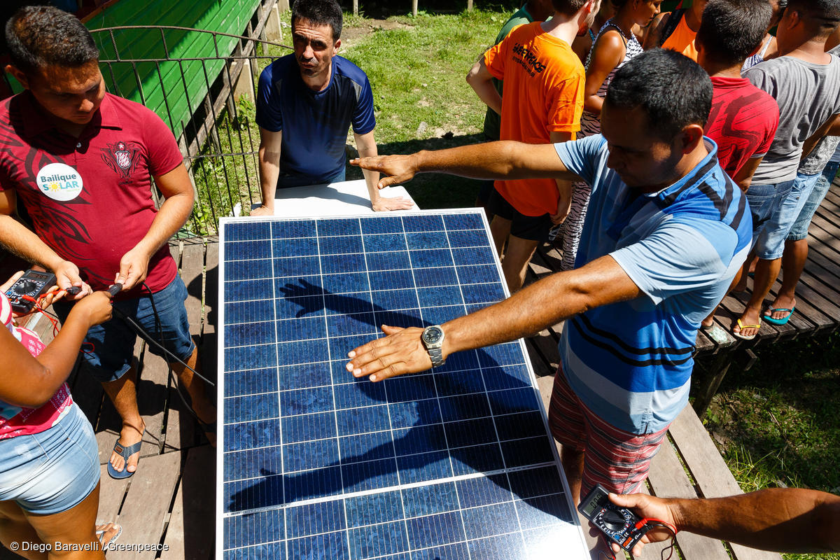Foto mostra moradores ao lado de placa solar recebendo capacitação sobre energia solar