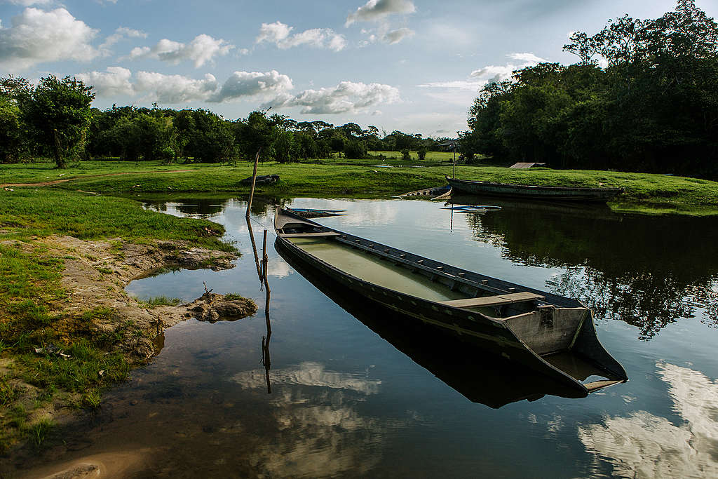 Imagem mostra lago com canoa e ao fundo comunidade