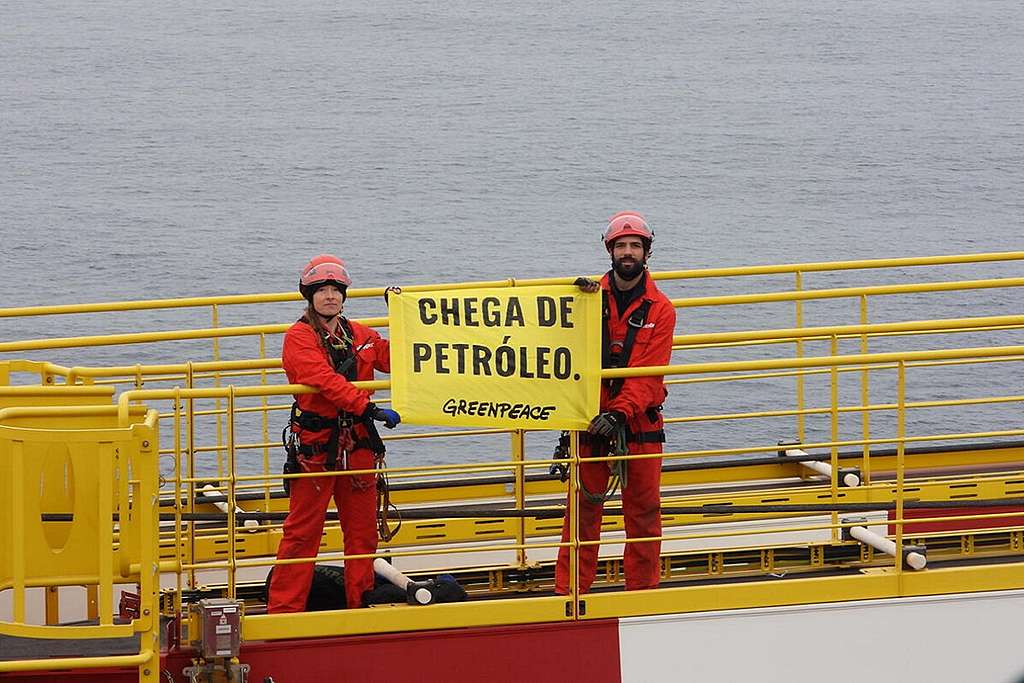 Ativistas que ocupam plataforma da Shell erguem banner com a mensagem "Chega de Petróleo", em português