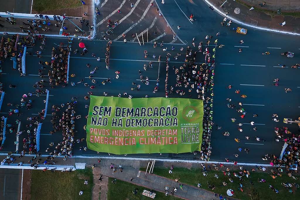 Marcha no Acampamento Terra Livre (ATL) com o banner escrito ''Sem demarcação não há democracia. Povos indígenas decretam emergência climática!'' 
