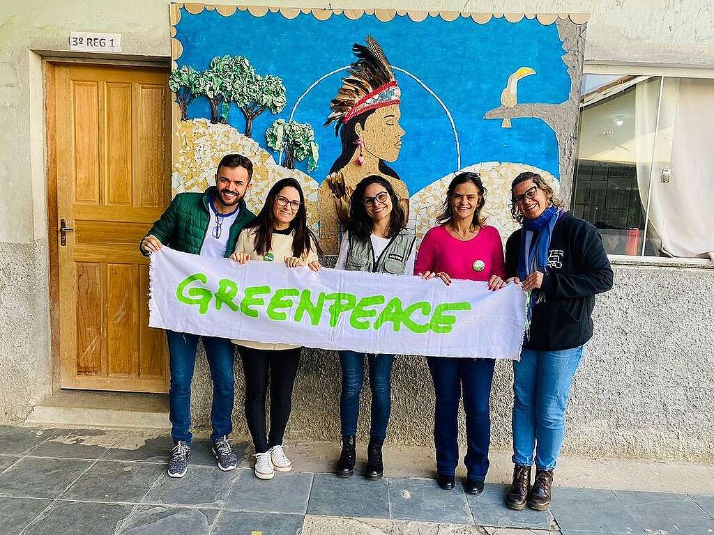 Foto de pessoas voluntárias em ambiente externo, eles e elas seguram o banner escrito Greenpeace