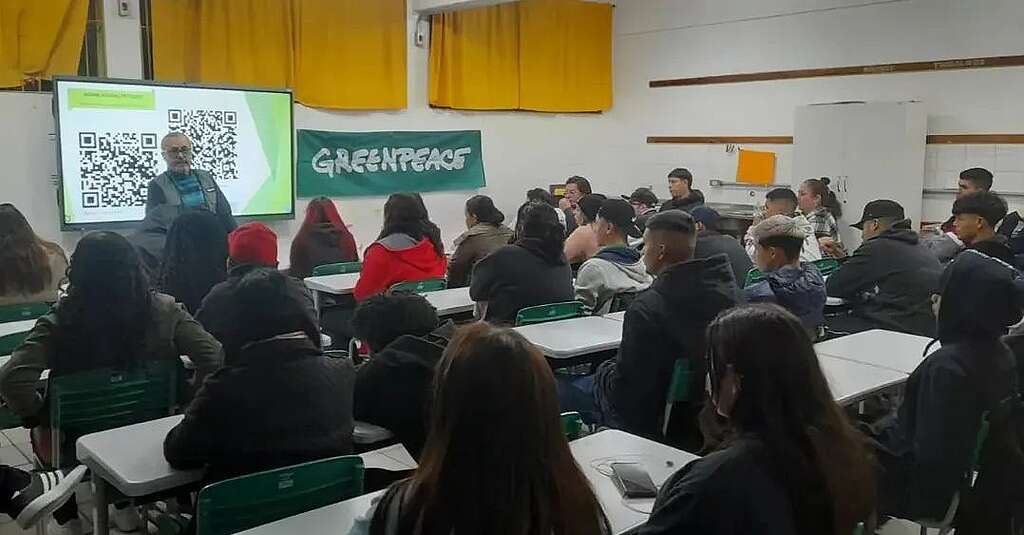 Foto de voluntário em sala de aula com dezenas de estudantes.