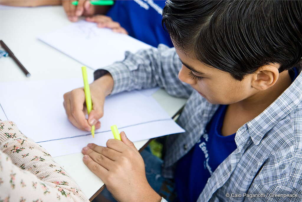 Em um plano fechado, mostra-se uma criança sentada em uma mesa colorindo um desenho.