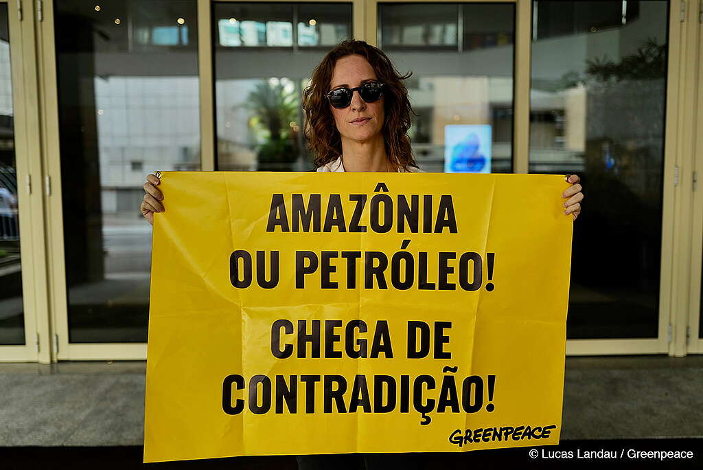 Laila Zaid, ativista ambiental e atriz, uma mulher branca e ruiva, usa óculos escuros e segura um banner amarelo com as frases: Amazônia ou petróleo! Chega de contradição!