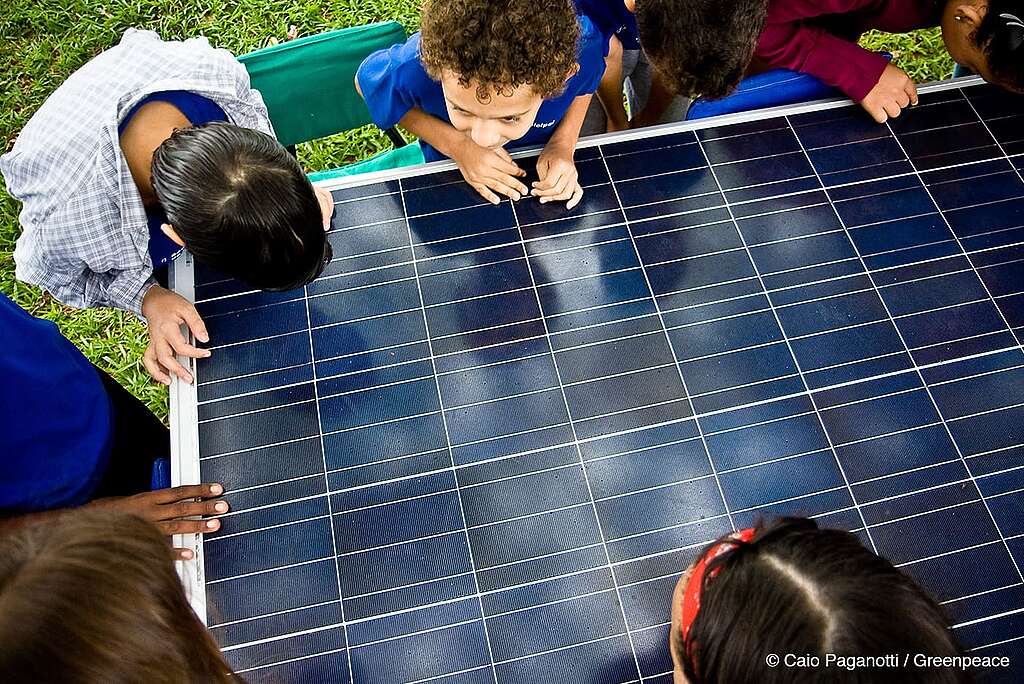 Foto de crianças em contato com uma placa de energia solar