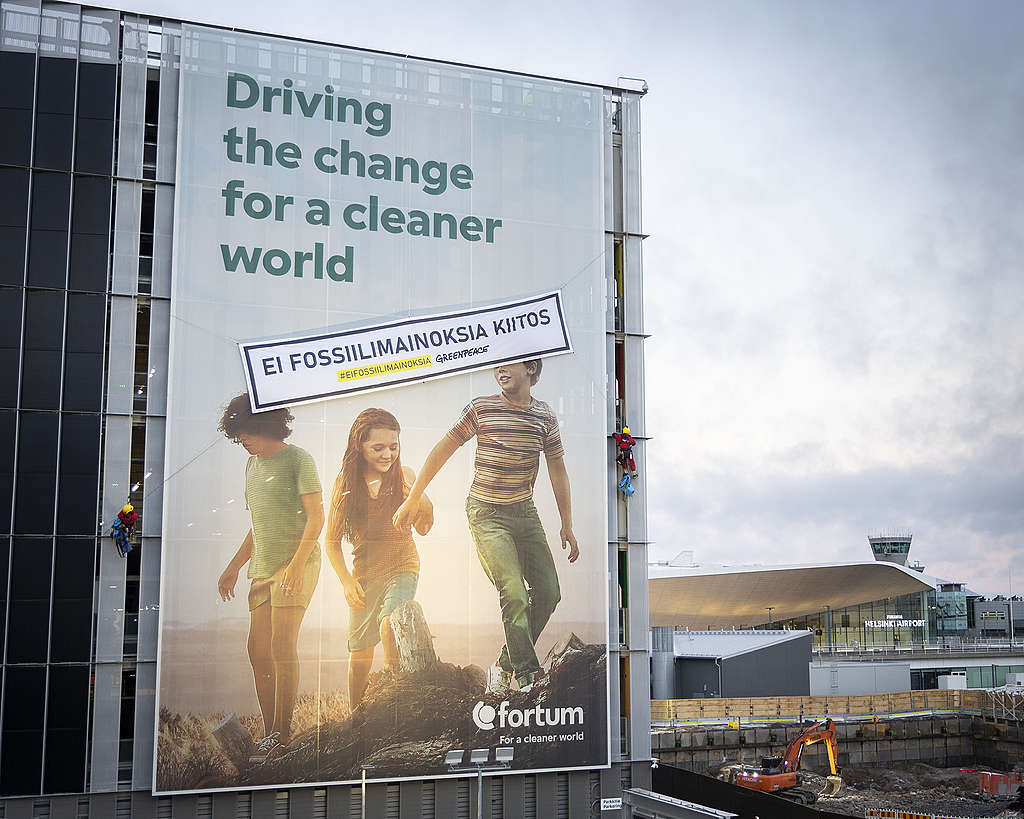 Greenpeacen aktivisit kiinnittivät fortumin mainokseen, jossa lukee "driving the change for a cleaner world" banderollin, jossa lukee "ei fossiilimainoksia, kiitos".