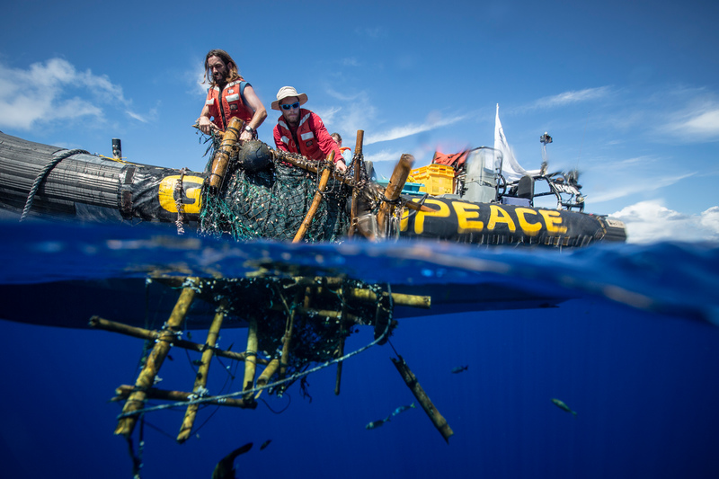 Kuvassa kaksi aktivistia nostavat pyydystä pois merestä Greenpeacen kumiveneeseen.