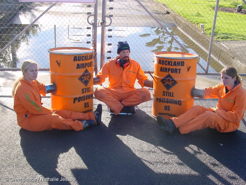 Greenpeace activists (from left to right) Sarah Duthie, Steve Abel and Suzette Jackson in protest at the Auckland Airport.  Greenpeace blocked trucks of quarantine and medical waste from entering the incinerator at Auckland International Airport (AIAL). Three activists locked themselves to barrels bolted into the ground to prevent trucks from entering the site. Two more activists hung a banner on the building reading "Stop Poisoning Us. Stop Incineration". Greenpeace demands that the facility will be replaced and that the New Zealand government bans incineration nationally. Dioxins are among the most poisonous substances known and there is no proven safe level of emissions. They are a by- product of the incineration process, and are not created by other waste disposal methods, such as steam sterilisation.