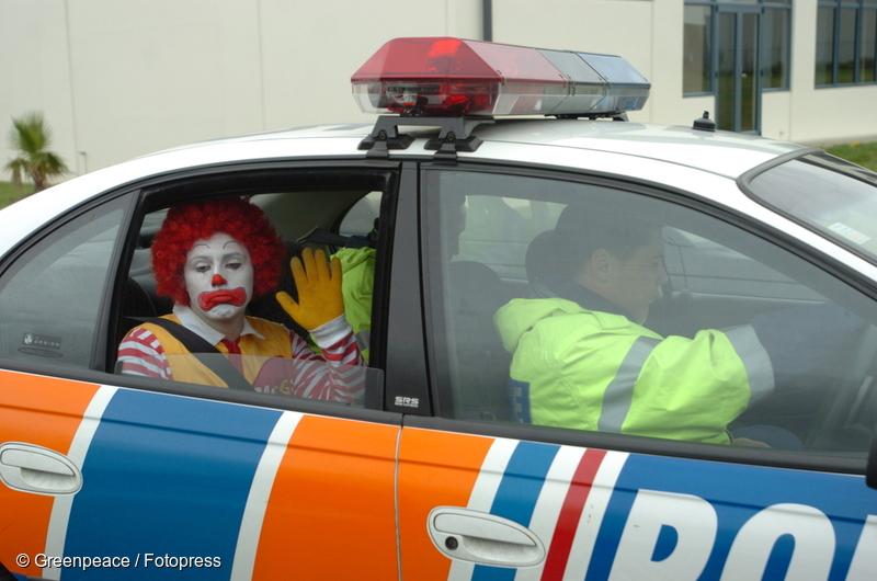 Greenpeace activist Gareth Hughes dressed as ‘Ronald McDonald’ being driven away by police after his arrest for chaining himself to the gates of McDonalds’ distribution centre in Wiri, Auckland, 11 May 2004