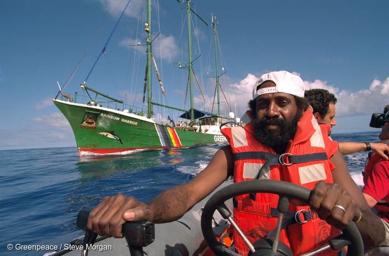 Rainbow Warrior crew member Philip Pupuka driving one of the inflatable boats flanked by SV Rainbow Warrior off Moruroa