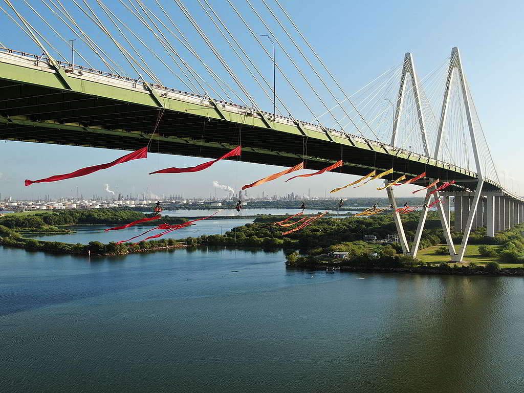 去年9月，22位綠色和平行動者垂吊於休斯敦Fred Hartman大橋，在這個化石燃料運輸幹道讓象徵可再生能源與可持續發展的旗幟飄揚。© Greenpeace