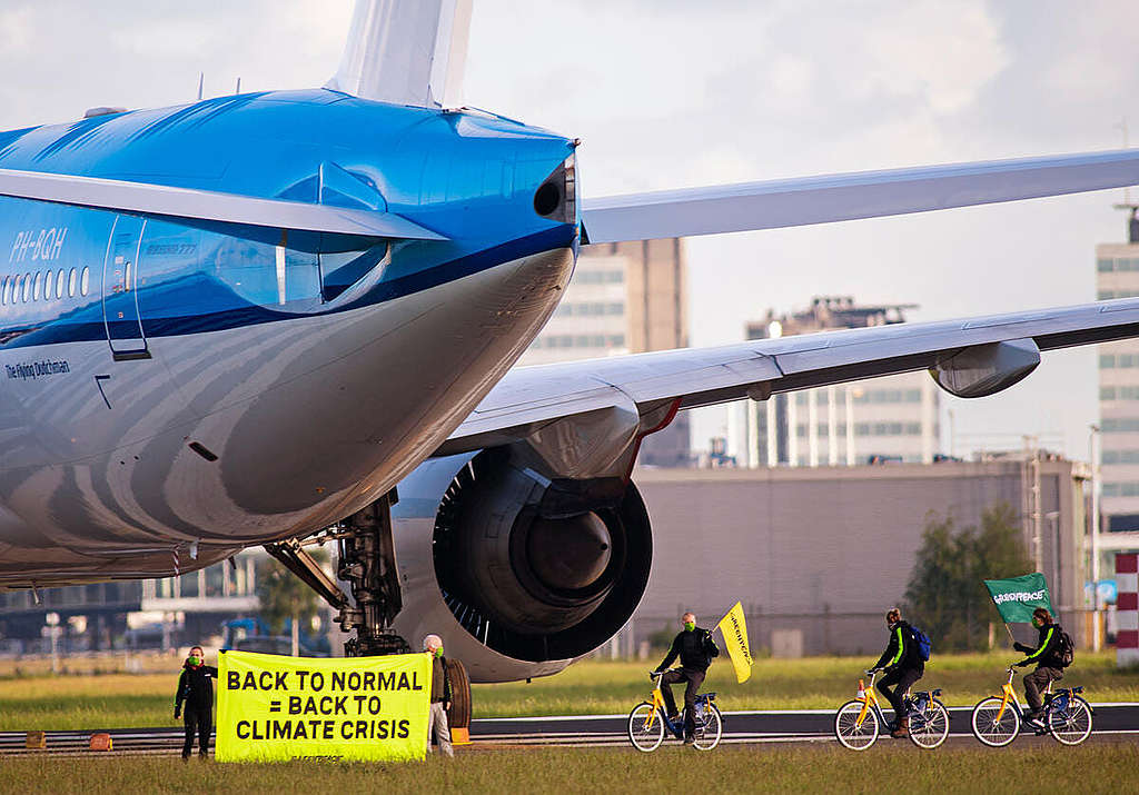 2020 年 5 月，綠色和平行動者踩單車進入史基浦機場，於一架荷蘭皇家航空客機前展示標語，促請當局在規模達數十億歐元的紓困方案，針對高碳排企業納入環保條款，避免進一步深陷氣候危機。 © Marten van Dijl / Greenpeace