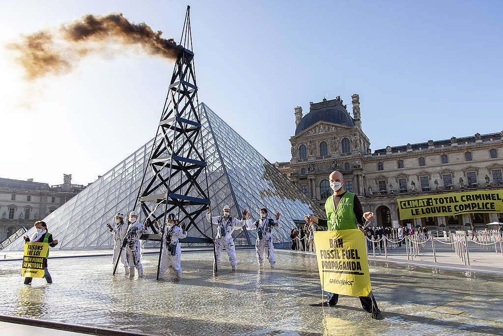 Several Greenpeace France activists protest in front of the Louvre museum in Paris to denounce the museum's complicity with the oil major TotalEnergies. They stand in front of the Louvre pyramid with banners “Let's make a law for a world without oil” and “Ban fossil fuel propaganda”.