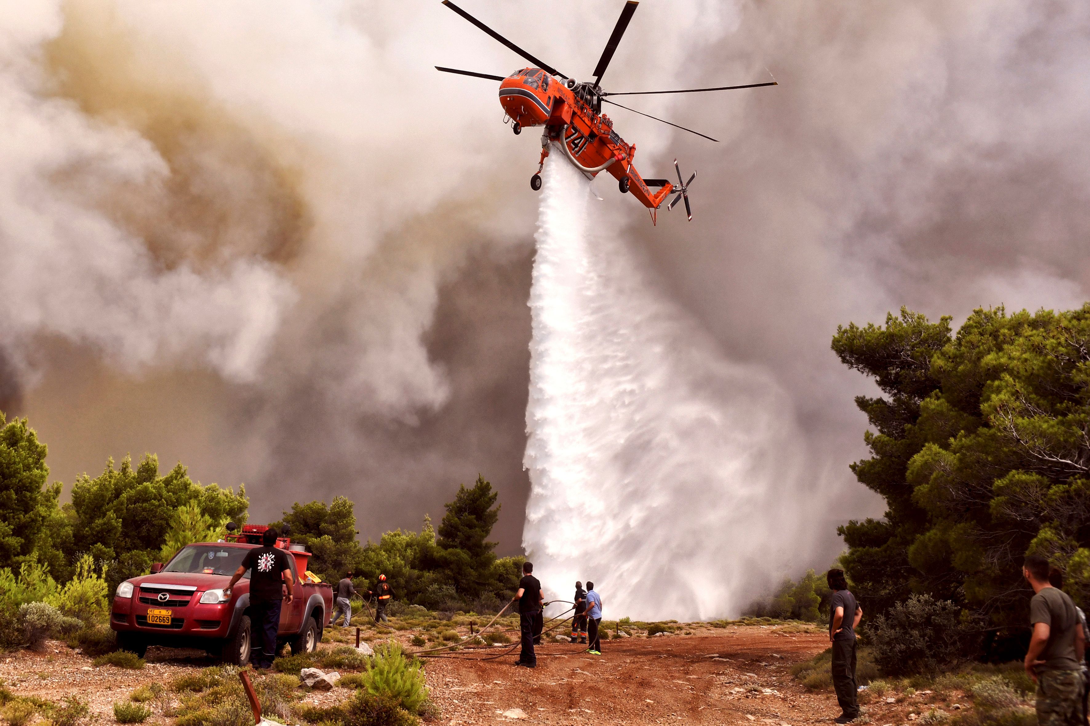A firefighting helicopter drops water to extinguish flames during a wildfire at the village of Kineta, near Athens. Photo: VALERIE GACHE/AFP/Getty Images
