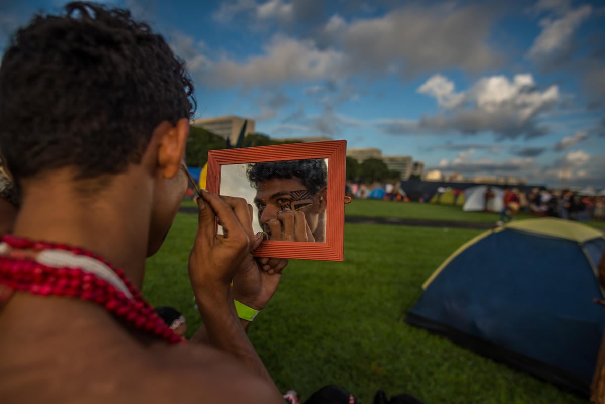 An Indigenous man paints himself at the Free Land Camp, the largest Indigenous mobilisation in the world. © Christian Braga / MNI