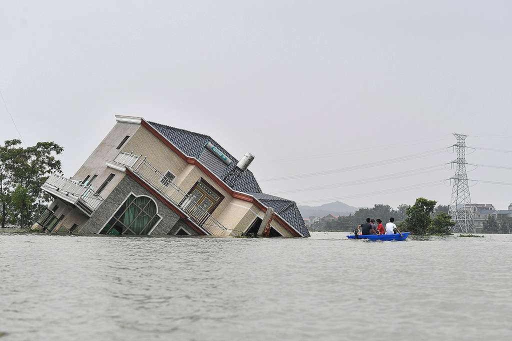 Residents riding a boat past a damaged and flood-affected house near the Poyang Lake due to torrential rains in Poyang county, Shangrao city in China's central Jiangxi province.  © STR/AFP via Getty Images© STR/AFP via Getty Images