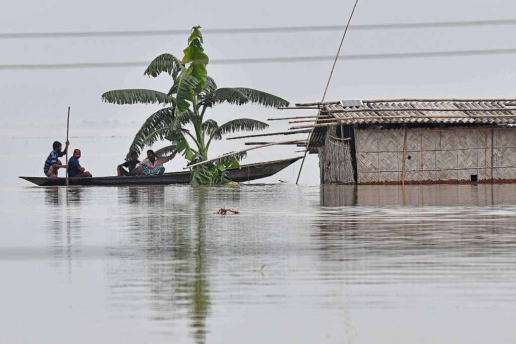 Villagers paddle their boat next to a partially submerged hut in the flood affected area of Hatishila, in Kamrup district of Assam state. © BIJU BORO/AFP via Getty Images