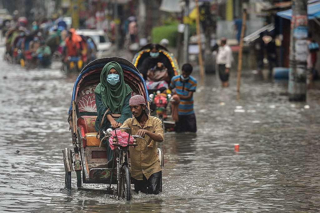 Cycle rickshaw pullers wade through a waterlogged street carrying their passengers after a heavy downpour in Dhaka, Bangladesh. © Munir Uz Zaman/AFP via Getty Images