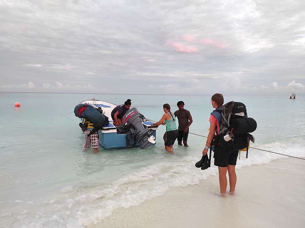 A group of young people on the beach, in bright and brown shirts, bring in a blue and white boat. © Emma Mederic