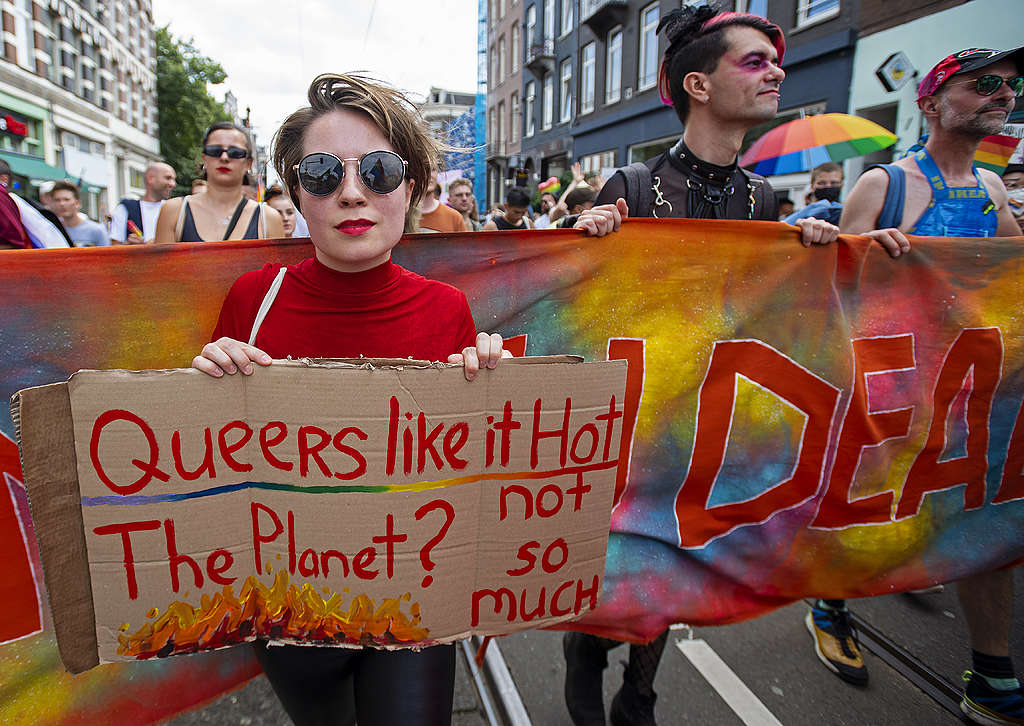 Picture showing a Queers4Climate activists standing against climate breakdown and holding a sign reading "Queers like it hot. The planet? Not so much."