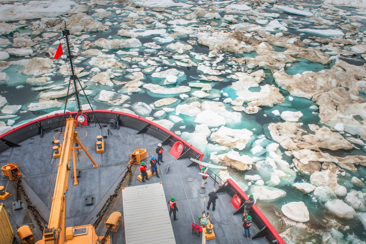 A drone shot of a US Coast Guard ship with men on deck is in Beaufort Sea with floating ice chunks.