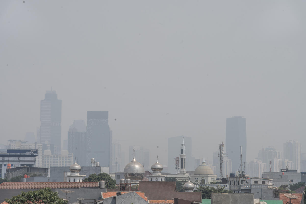 A mosque, houses and in the background tall buildings are covered by smog from air pollution in Jakarta