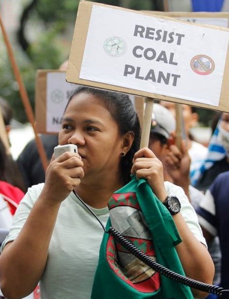 A girl speaking into a microphone and holding a sign that says Resist Coal Plant