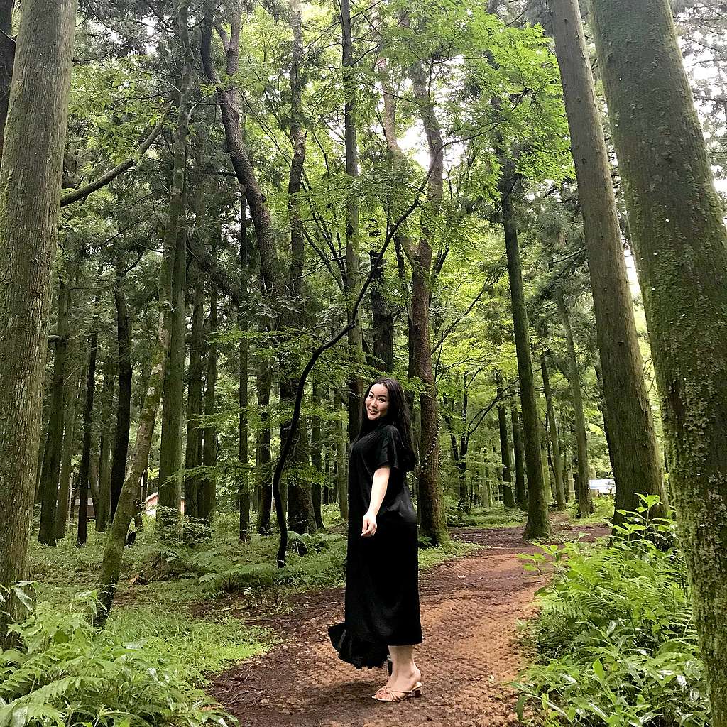 A girl in a long black dress standing on a pathway surrounded by trees