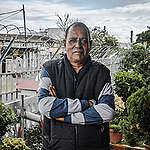 Veteran environmental justice activist and co-ordinator of the South Durban Community Environmental Alliance (SDCEA) Desmond D’Sa stands on the veranda of the organisation’s offices. His home can be seen behind him and smokestacks of another refinery behind that.