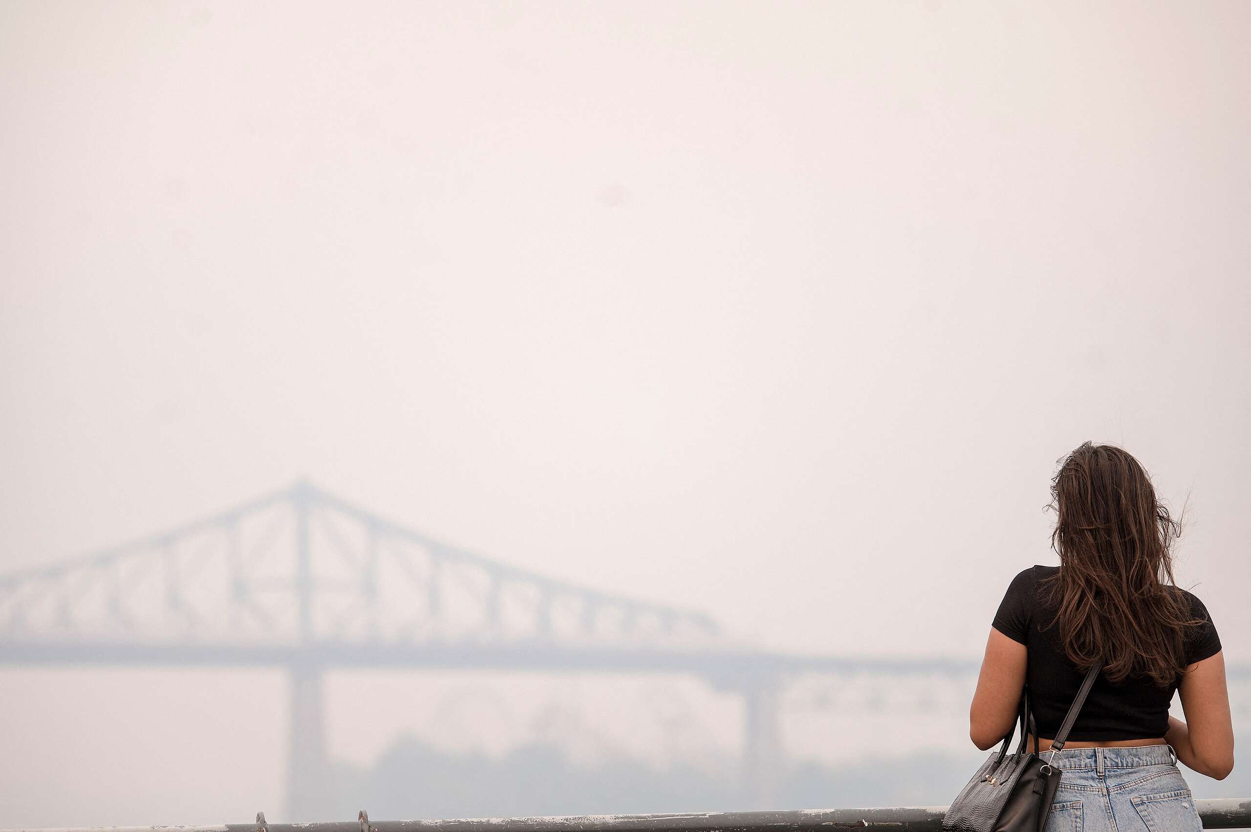 A woman looks at the Jacques-Cartier Bridge through the smoke caused by the wildfires in Northern Quebec in Montreal, Quebec, on June 25, 2023. Montreal had the worst air quality in the world according to IQ Air. Environment Canada issued a Smog warning because of the smoke and discouraged exercise and spending too long outdoors. © ANDREJ IVANOV/AFP via Getty Images