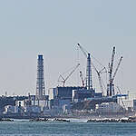 Distant view of the Fukushima Daiichi Nuclear Power Station from Ukedo port. The central frame is Unit 1, while the structure behind it that appears to overlap is the Unit 2. The dome roof further behind is the Unit 3, and the slightly visible building cover on the left represents the Unit 4.