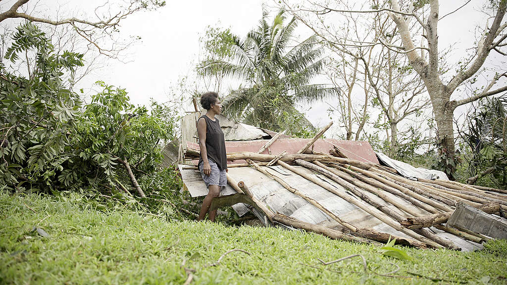 A woman stands in front of her home which is in ruins after a cyclone.